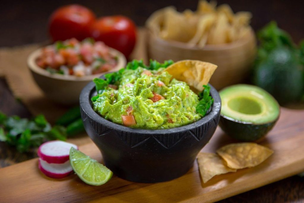 guacamole accompanied by tortilla chips and tomato, in a typical Mexican molcajete
