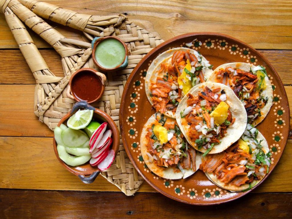 pastor tacos accompanied by green and red sauce, with cucumbers, radishes and lemons. Decorated with its traditional pineapple
